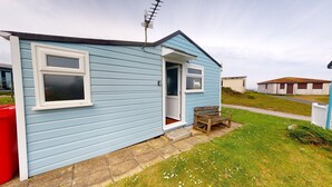 A small, single-story house with a light blue exterior, a front door, and a small porch with a bench.