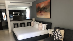 A modern hotel room with a large bed, a sofa, a coffee table, and a kitchen area with a bar. - Aldea Thai jr suite. Or Studio By OceanFront  for upto 4 pax  (Playa del Carmen)