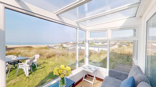 A conservatory with a view of a grassy area and houses. - C35 Le Grace, Riviere Towans (Hayle)