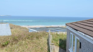 A coastal view with a beach, a building with a sloped roof, and a clear sky. - C35 Le Grace, Riviere Towans (Hayle)