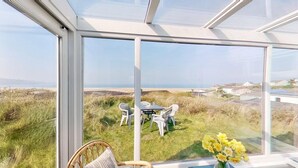 A conservatory with a glass wall overlooking a grassy area with a table and chairs. - C35 Le Grace, Riviere Towans (Hayle)