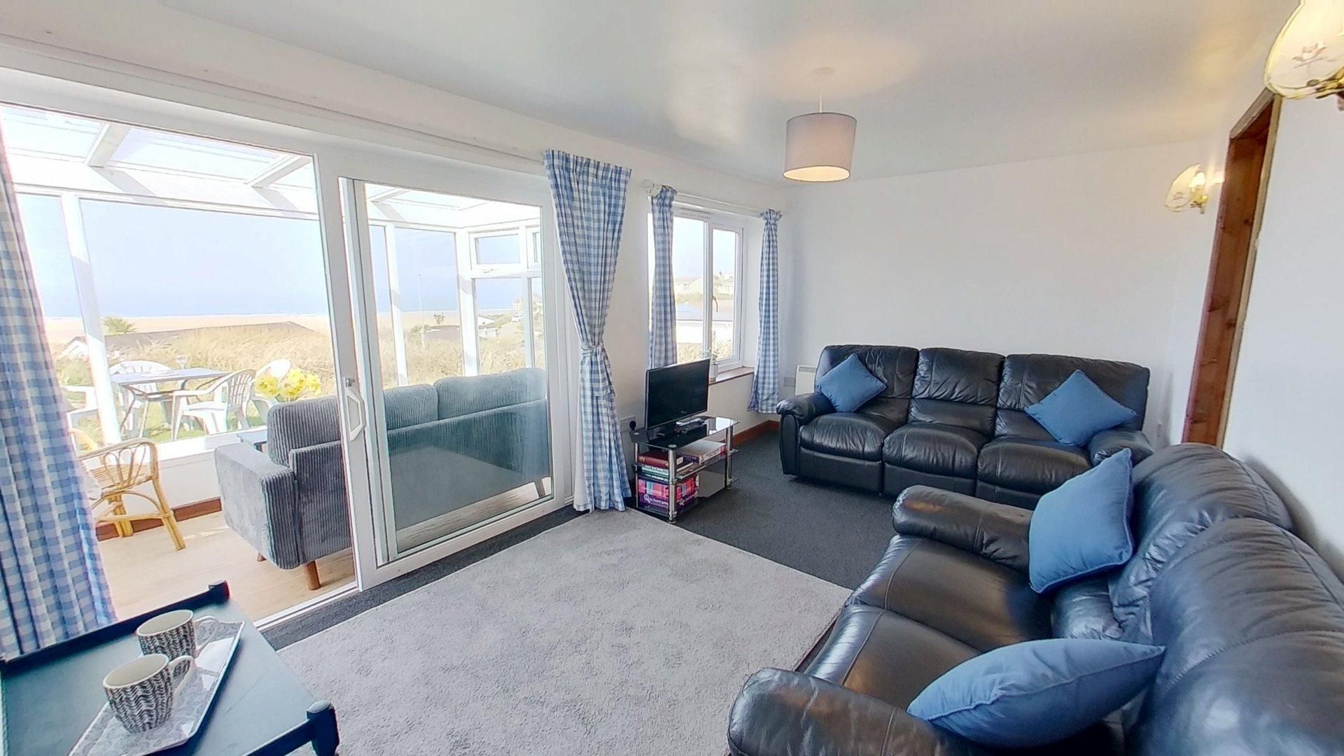 A living room with a black leather sofa, a television, and a balcony with checkered curtains.