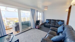 A living room with a black leather sofa, a television, and a balcony with checkered curtains. - C35 Le Grace, Riviere Towans (Hayle)