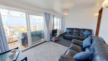 A living room with a black leather sofa, a television, and a balcony with checkered curtains.