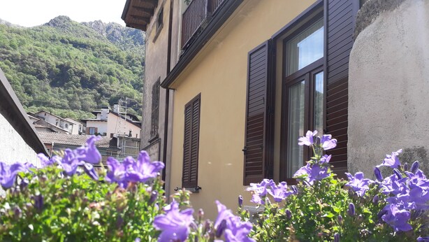A building with a balcony, a window with shutters, and a flower box with purple flowers. - La CasaLina - tourist rental (Omegna)
