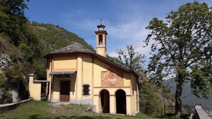 A small, yellow church with a bell tower and arched entrance, surrounded by greenery and hills. - La CasaLina - tourist rental (Omegna)