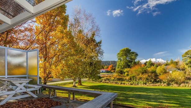 A wooden deck with a table and benches, overlooking a grassy area with trees and a distant mountain.