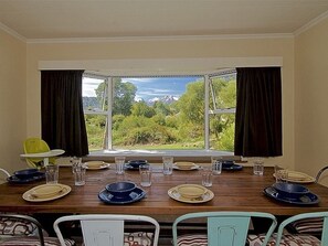 A dining area with a table set for four, a view of greenery and mountains through a window, and a yellow chair.