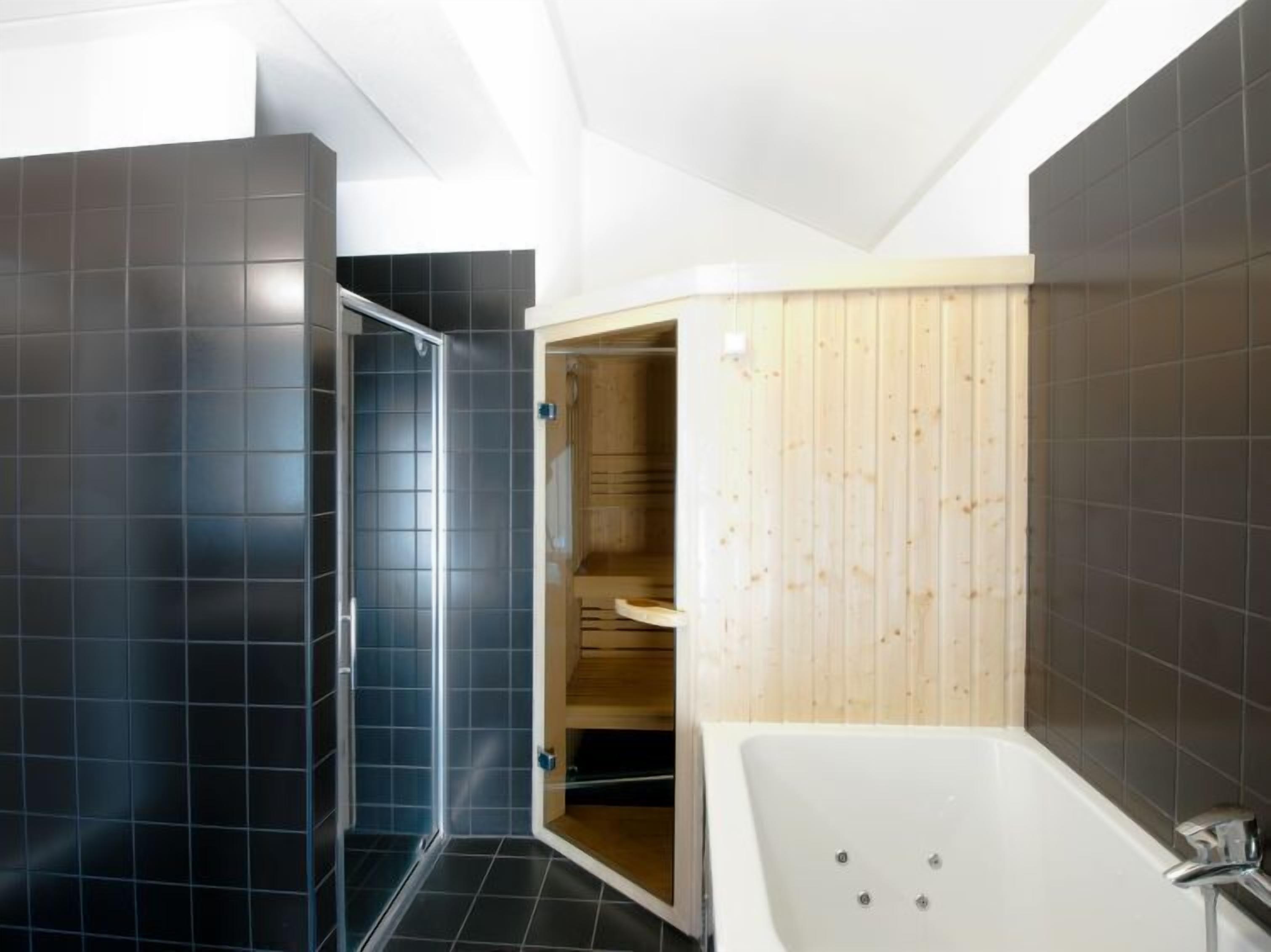 A modern bathroom with a large bathtub, a shower area, and wooden paneling on one wall.