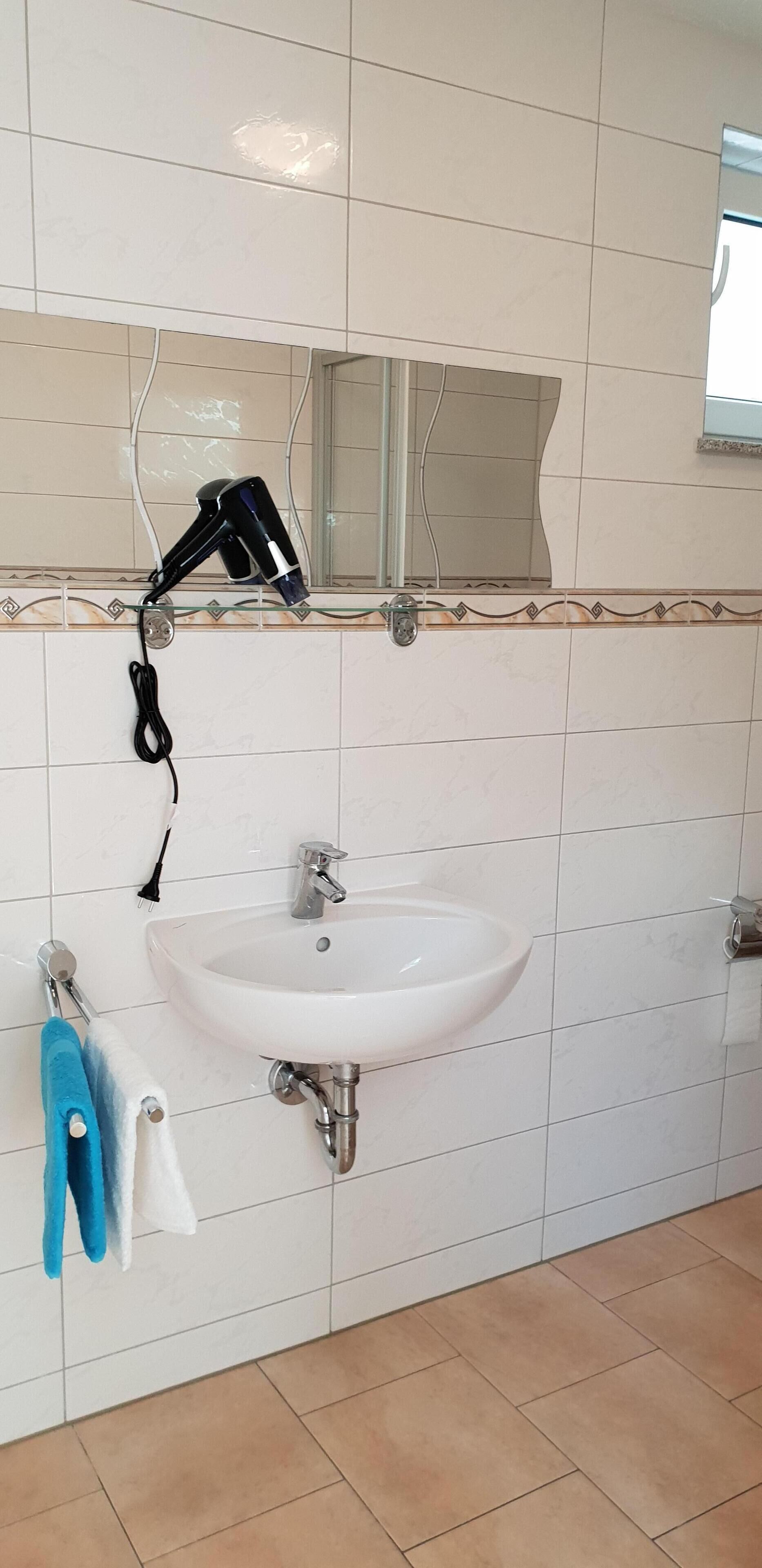 Un bany amb un lavabo blanc, un assecador i dues tovalloles penjades a la paret.