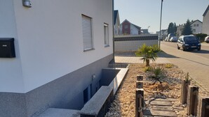 Een woonstraat met een wit huis, een kleine tuin met kiezels en beplanting, en geparkeerde auto's.