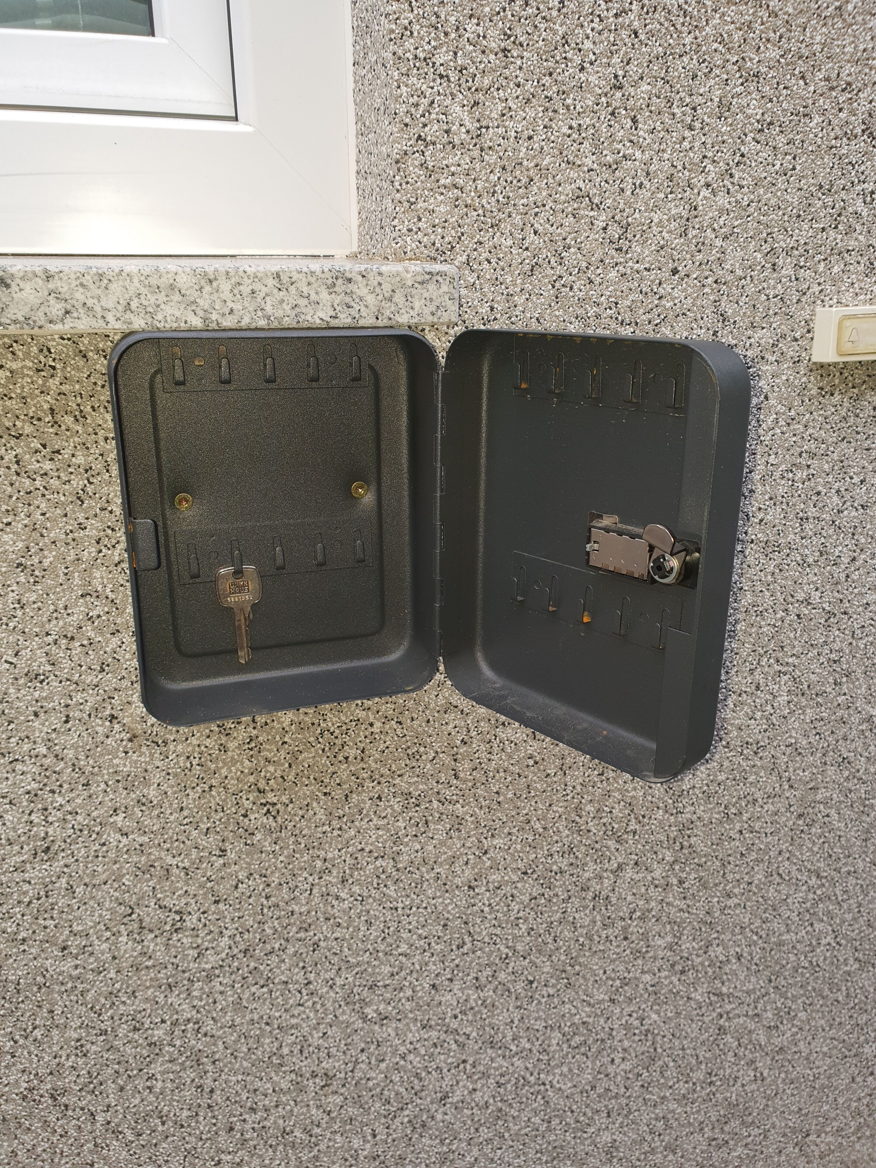 Un système d’interphone noir, doté d’un clavier et d’une serrure, fixé sur un mur à texture.