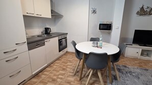 Een compacte keuken met een magnetron, fornuis en spoelbak. Er is een eettafel met stoelen en een flatscreen televisie op een standaard.
