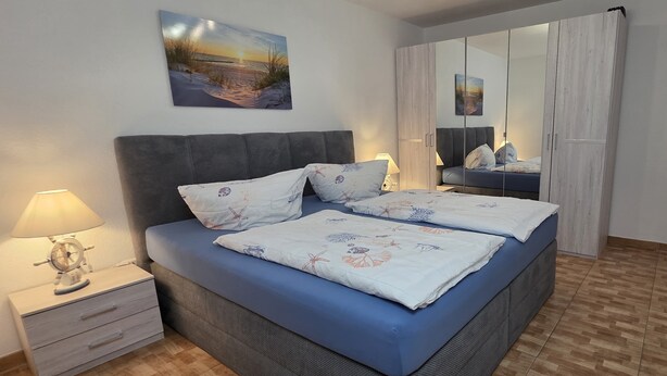 Een slaapkamer met een bed, nachtkastje, lamp en een schilderij aan de muur.