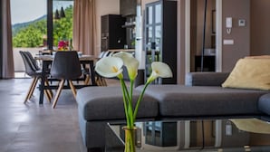 Uma sala de estar moderna com um sofá cinzento, uma mesa de centro de vidro e um vaso com flores brancas.