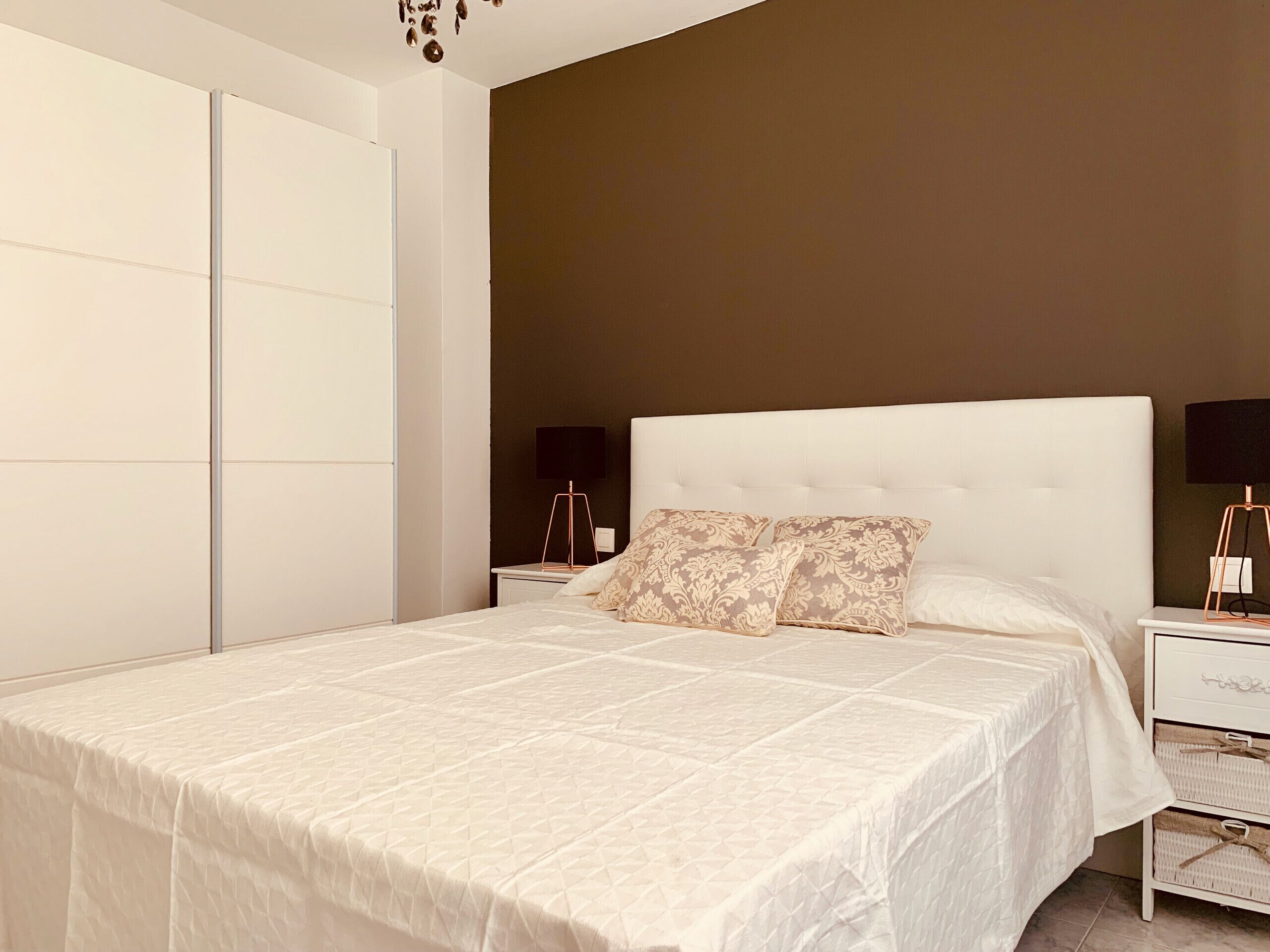 A bedroom with a large bed, a bedside table, a nightstand, and a wardrobe.