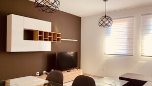 A modern living room with a flat-screen TV, a glass dining table, and a built-in wooden shelf unit. - A&F Comfort Modern House (Santa Lucía de Tirajana)