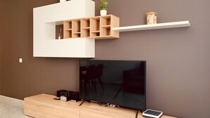 A modern living room with a flat-screen TV, wooden entertainment unit, and a white shelf with decorative items. - A&F Comfort Modern House (Santa Lucía de Tirajana)