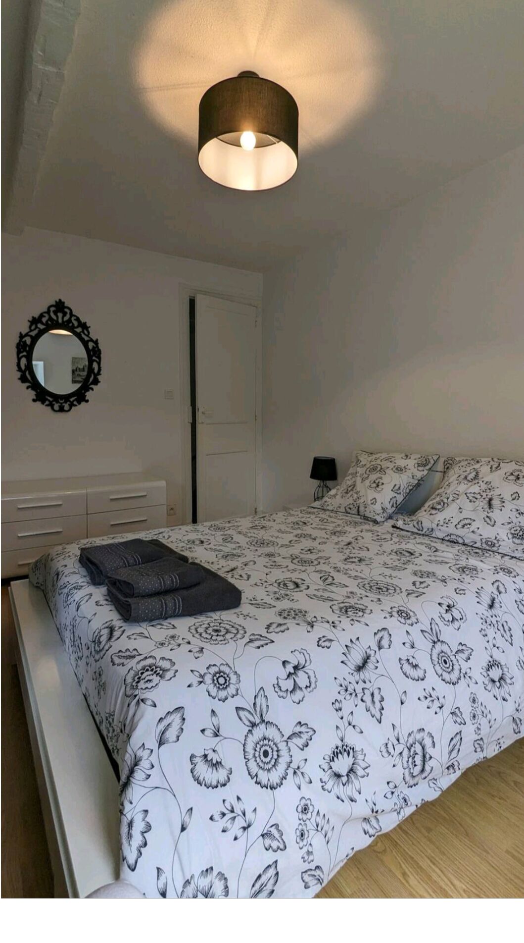 Een slaapkamer met een bed, een nachtkastje, een lamp, een spiegel en een plafondarmatuur.