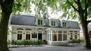 A two-story building with a tiled roof, large windows, and a sign that reads "BOSCHLUST". - BERGEN: 'Boschlust', beautiful apartments in country house style and close to the beach! (Bergen)