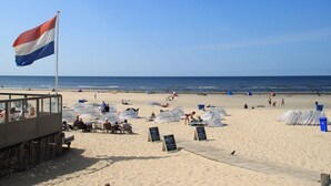 A beach with a flag, umbrellas, and a food stand. - BERGEN: 'Boschlust', beautiful apartments in country house style and close to the beach! (Bergen)