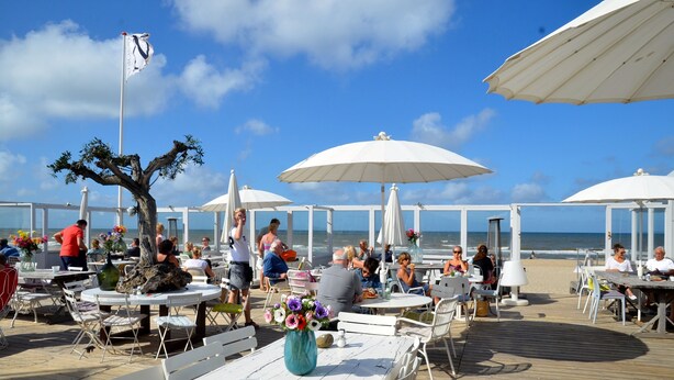 An outdoor dining area with white tables and umbrellas, overlooking the beach. - BERGEN: 'Boschlust', beautiful apartments in country house style and close to the beach! (Bergen)