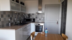 A modern kitchen with a microwave, coffee maker, and Bosch oven. There is a wooden table with a water bottle and bread. - New apartment with terrace view and sea access 2 people all comfort / bicycles (Saint-Jean-de-la-Rivière)