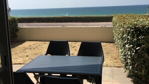 A patio with two chairs and a table, overlooking a beach and a road. - New apartment with terrace view and sea access 2 people all comfort / bicycles (Saint-Jean-de-la-Rivière)