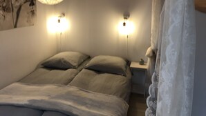 Une chambre à coucher avec un lit, deux lampes de chevet, une table de nuit et un mur orné d’un tableau représentant des motifs floraux.