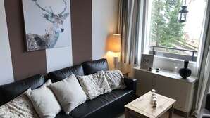 Un salon moderne avec un canapé en cuir noir, des coussins à motifs, une table basse en bois et une fenêtre avec des rideaux.