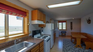Una cocina moderna con armarios de madera, una estufa empotrada y un amplio ventanal con un visillo rojo.