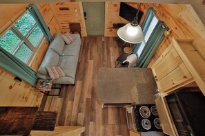 Interior de una cabaña con sofá, mesa de comedor, televisor y zona de cocina.