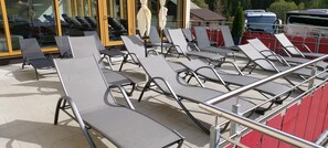 A row of sun loungers with metal frames and grey mesh seats, arranged in a patio area with a tiled floor.