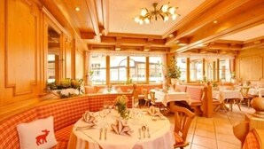 A restaurant with wooden paneling, large windows, and a chandelier. Tables are set with white tablecloths and silverware. - Modern furnishings, balcony. wonderful mountain view summer - mountain railway ticket inc. (Mittelberg)