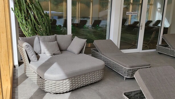 A modern outdoor lounge area with a large cushioned seating area and multiple lounge chairs. - Modern furnishings, balcony. wonderful mountain view summer - mountain railway ticket inc. (Mittelberg)