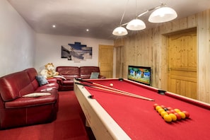 A pool table with balls, a red sofa, a television, and wooden paneling.