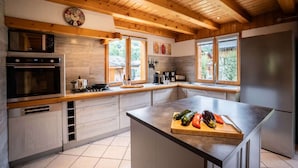 A modern kitchen with wooden beams, a large island, and a view of the outdoors. - Chalet Snow Paradise (Les Belleville)