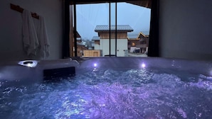 A modern spa room with a hot tub, large windows, and a view of traditional buildings outside. - Chalet Snow Paradise (Les Belleville)