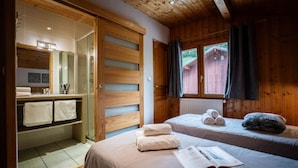 A bedroom with a bed, a window with curtains, a wooden wardrobe, and a bathroom with a glass shower. - Chalet Snow Paradise (Les Belleville)