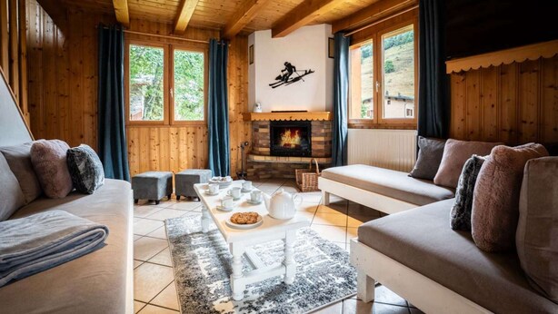 A cozy living room with wooden walls and ceiling, a fireplace, and large windows offering a view of the outdoors. - Chalet Snow Paradise (Les Belleville)