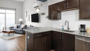 A modern kitchen with dark wood cabinets, a granite countertop, and a built-in dishwasher. - Studio King Suite with Kitchen | 300 (Asheville)