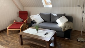 A cozy living room with a wooden floor, a red chair, a grey sofa, and a small table with a remote control. - "FeWo Tante Ju" with a view of the Bauhaus in Dessau-Roßlau (Dessau-Roßlau)