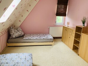 Une chambre avec un plafond en pente, un lit avec une literie à motifs, un radiateur, une armoire en bois et une fenêtre avec des stores.