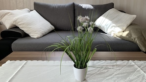 A modern living room with a grey sofa, white cushions, and a potted plant on a wooden table. - "FeWo Tante Ju" with a view of the Bauhaus in Dessau-Roßlau (Dessau-Roßlau)
