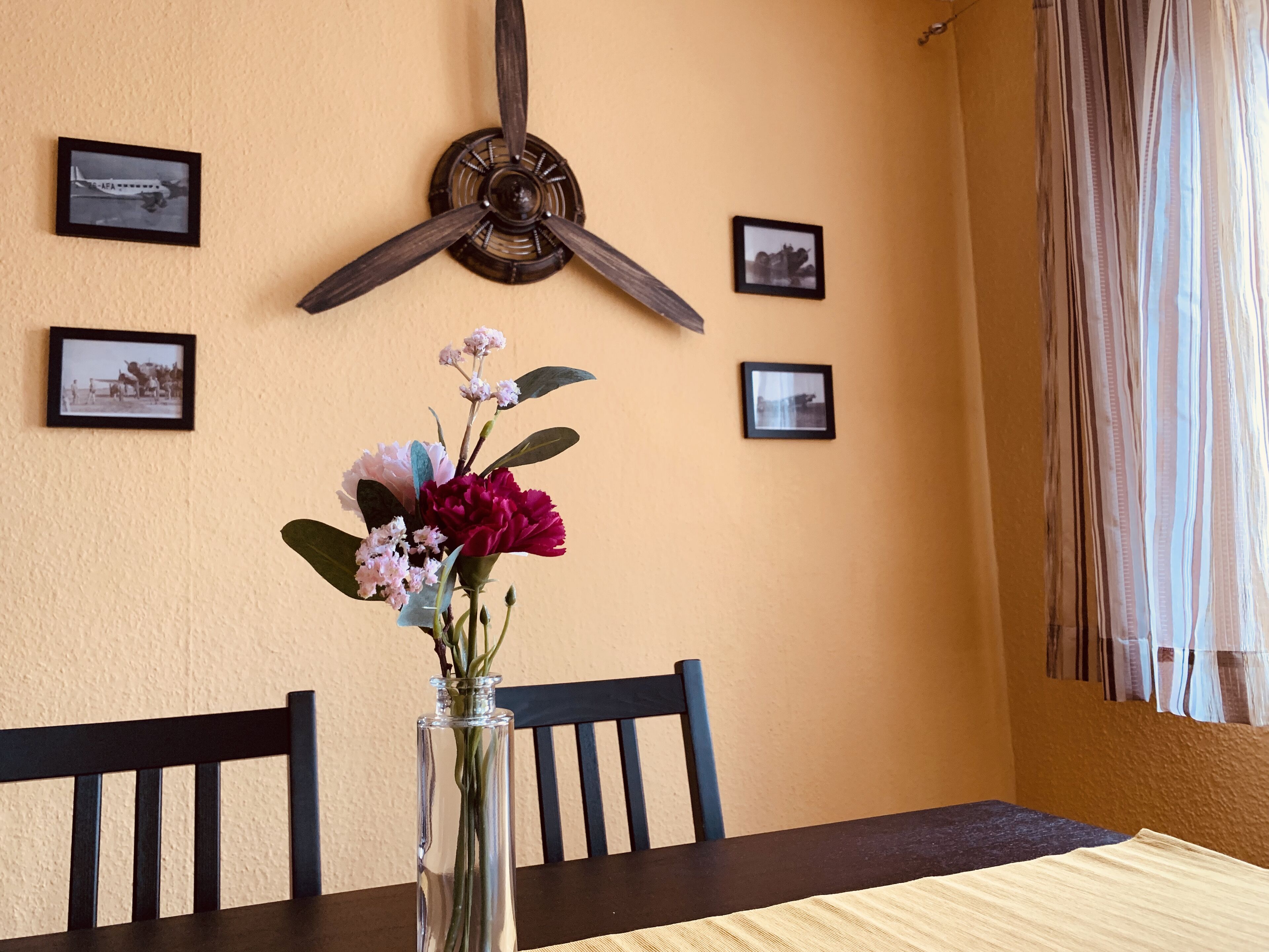Ein Essbereich mit Tisch, Stühlen, einer Blumenvase und gerahmten Bildern an der Wand.