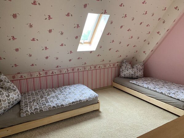 A small, cozy room with two bunk beds, a sloped ceiling, and a window providing natural light.