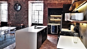 A modern kitchen with a large island, brick walls, exposed ceiling, and a clock on the wall. - Luxurious apartment in historic building  downtown Puebla SV311 -12 (PUEBLA)