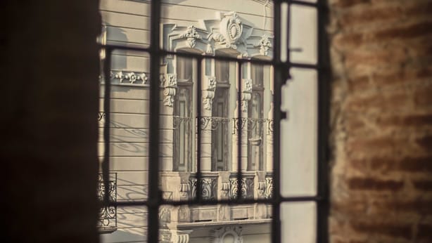A view through a window with ornate iron bars, featuring classical architectural details and a stone wall. - Luxurious apartment in historic building  downtown Puebla SV311 -12 (PUEBLA)