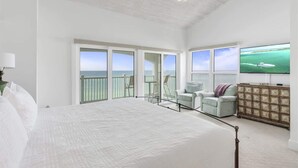 Ein geräumiges Schlafzimmer mit einem großen Bett, einem Balkon mit Meerblick und einem an der Wand befestigten Fernseher.