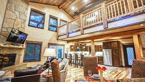 Un vaste espace de vie doté d’une cheminée en pierre, d’un plafond en bois et d’un balcon agrémenté d’une balustrade.